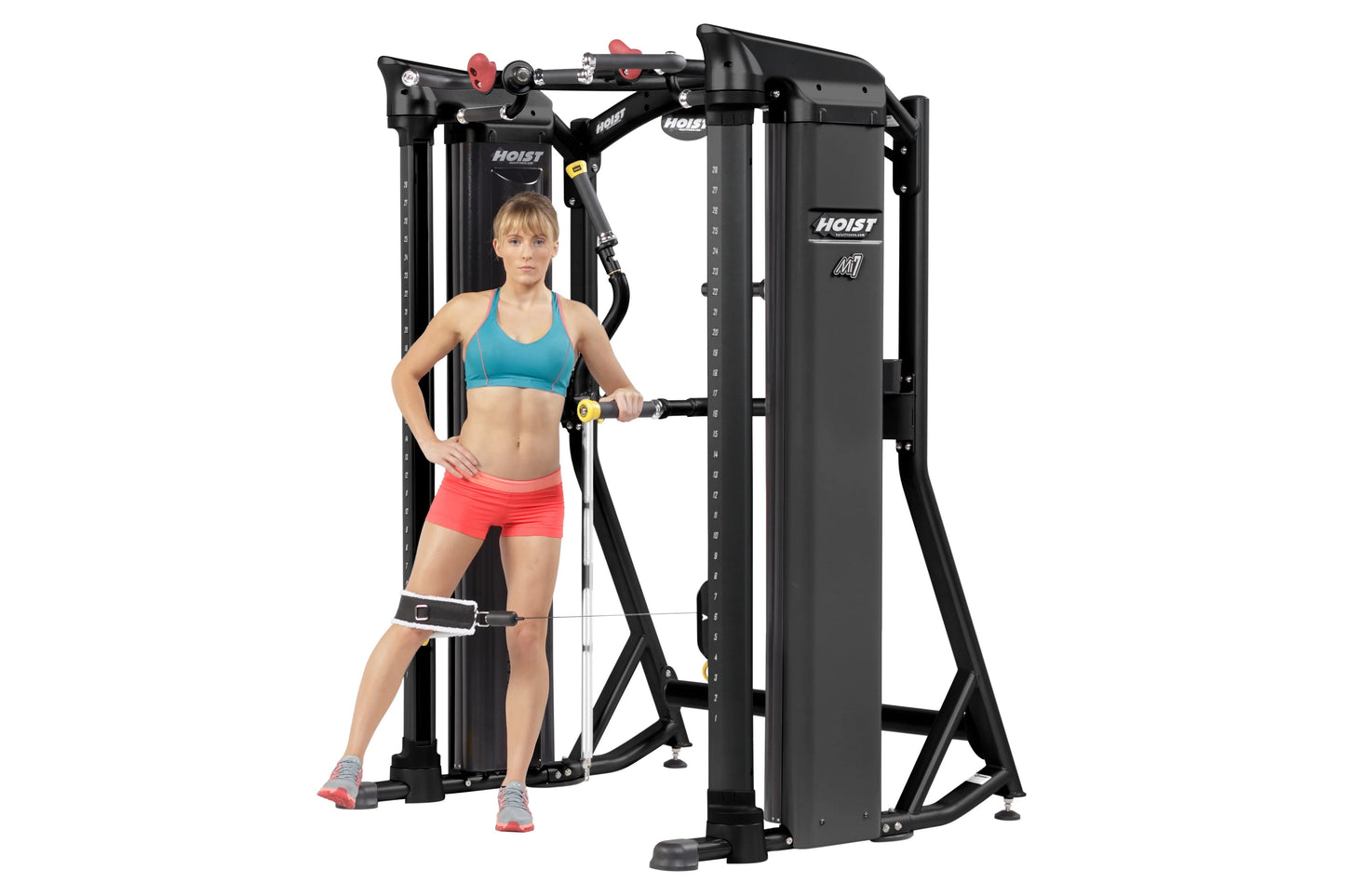 Black Hoist Mi7 functional training system with red adjustment knobs, worn by model in turquoise sports bra and coral shorts 