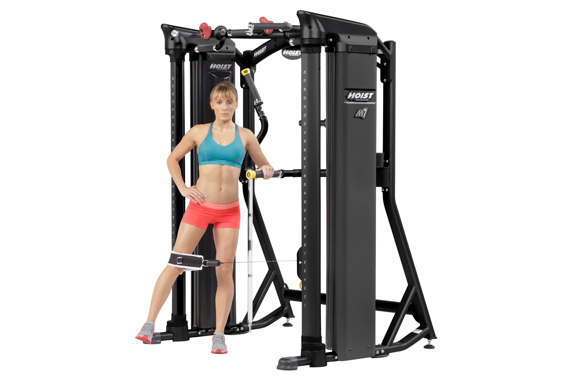 Black Hoist Mi7 functional training system with red adjustment knobs, worn by model in turquoise sports bra and coral shorts 