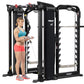 Woman in blue sports bra and coral shorts using Hoist MI7 black Smith machine with cable attachments and weight stack on whit