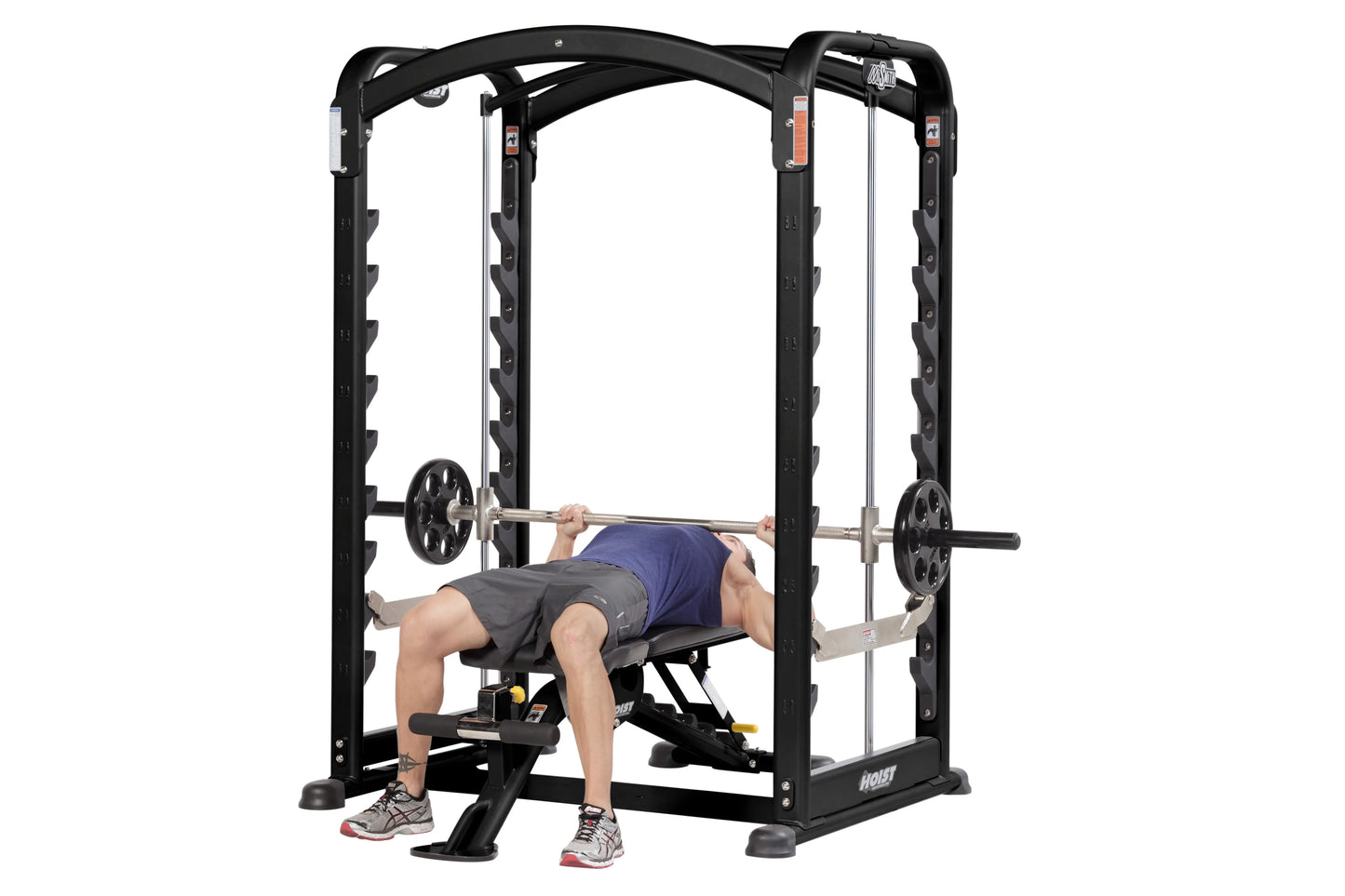 Black steel Smith machine with dual action rails, weight plates on barbell, and male model demonstrating bench press exercise