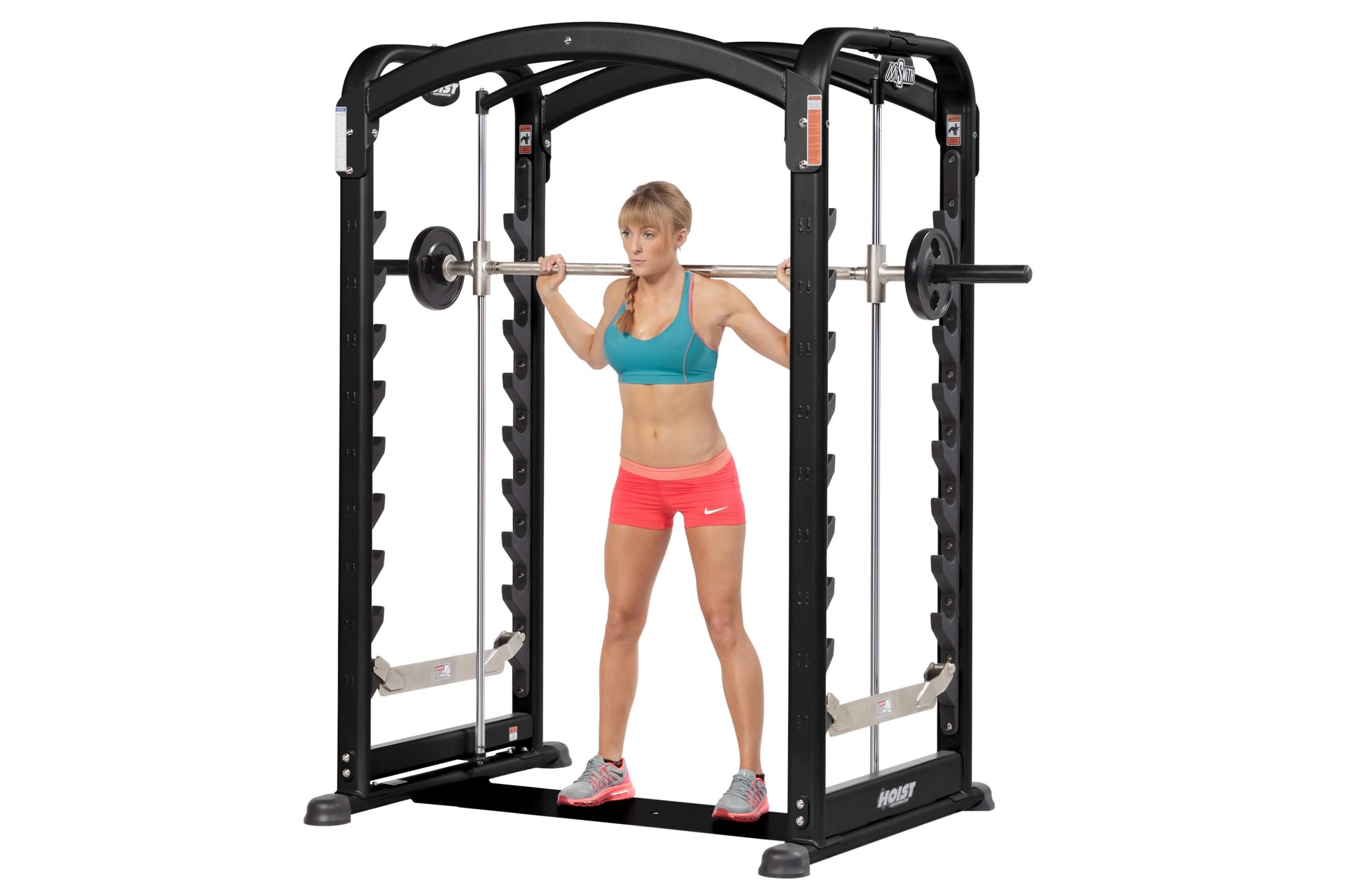 Black Hoist Smith machine with dual action arms, woman in teal sports bra and coral shorts using barbell, white background