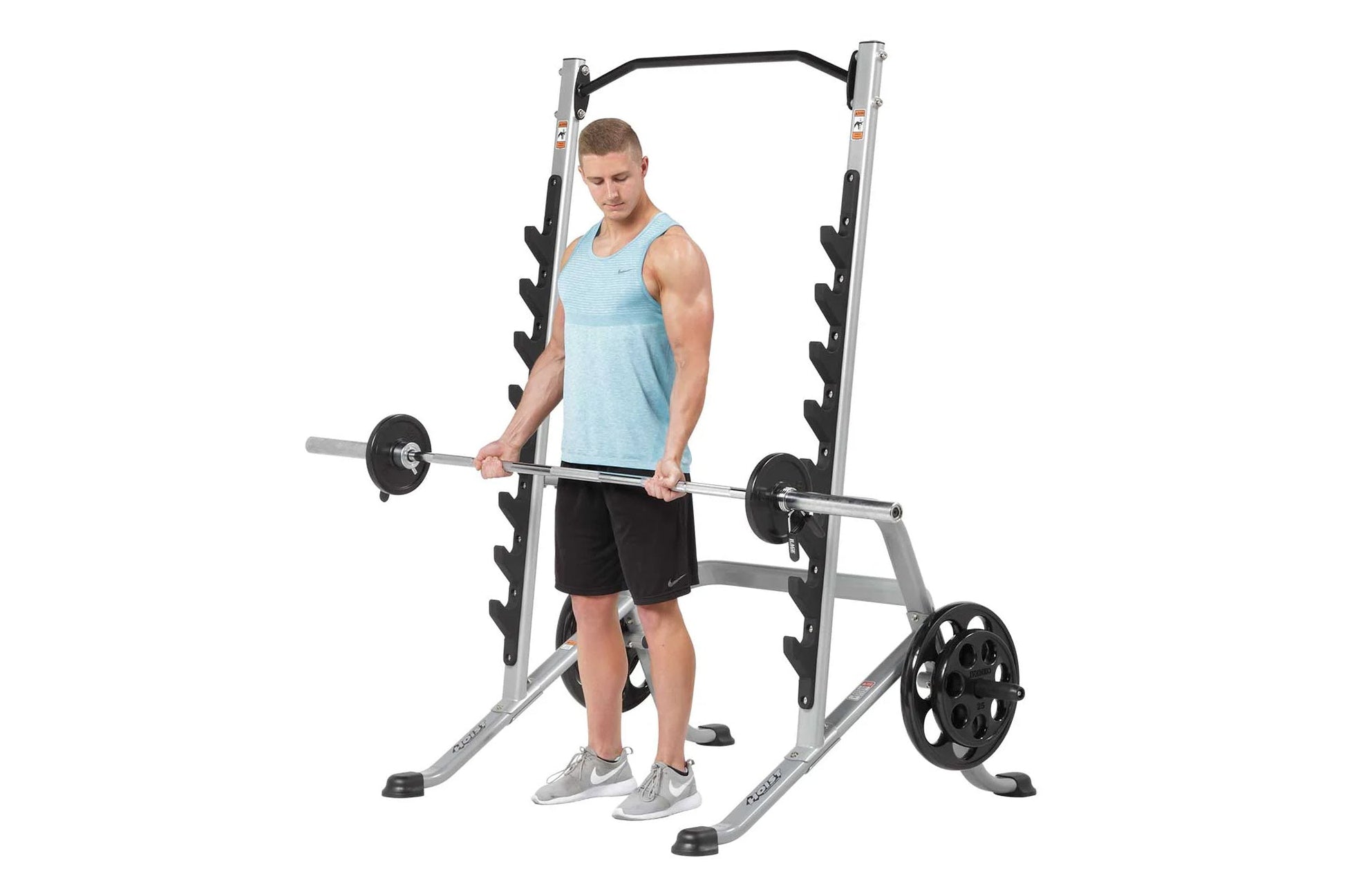 Male user demonstrating squat rack with barbell and weight plates, silver and black metal frame with dumbbell storage on whit