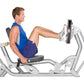 Man in blue tank top and navy shorts using silver Hoist ROC-IT leg press machine with foot pedal extended, on white backgroun