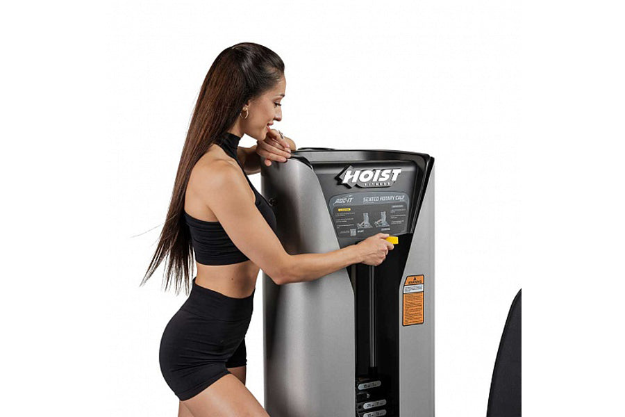 Woman in black sports bra and shorts using Hoist ROC-IT rotary calf machine with silver and black frame on white background