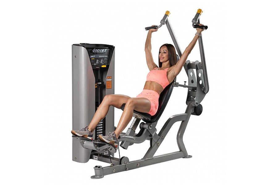 Woman in pink sports bra and shorts using gray Hoist shoulder press machine with overhead handles on white background
