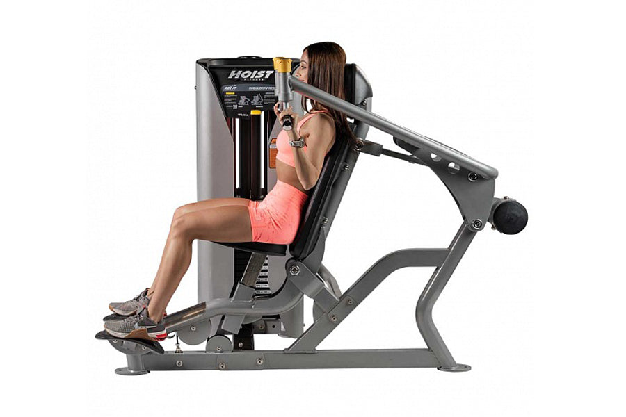Hoist ROC-IT shoulder press machine with gray frame and black upholstery, woman in coral tank top demonstrating seated exerci