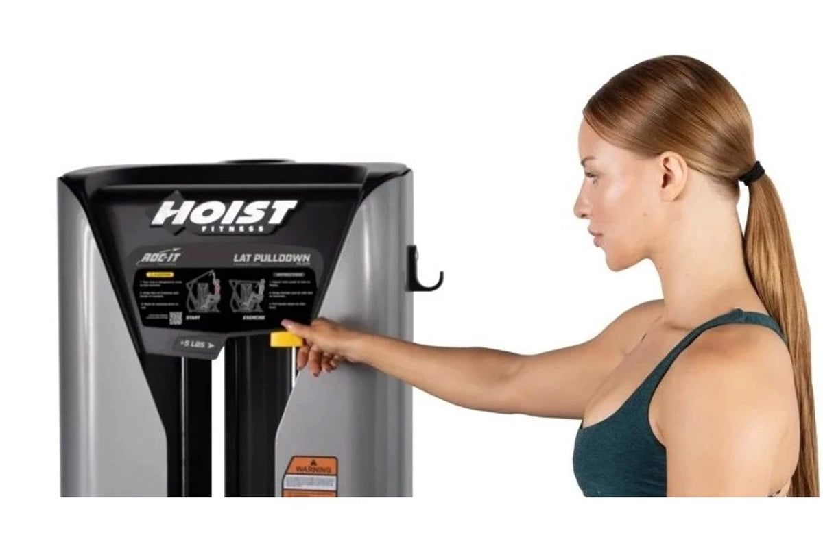 Woman in teal sports bra using Hoist ROC-IT black and silver lat pulldown machine with instruction panel