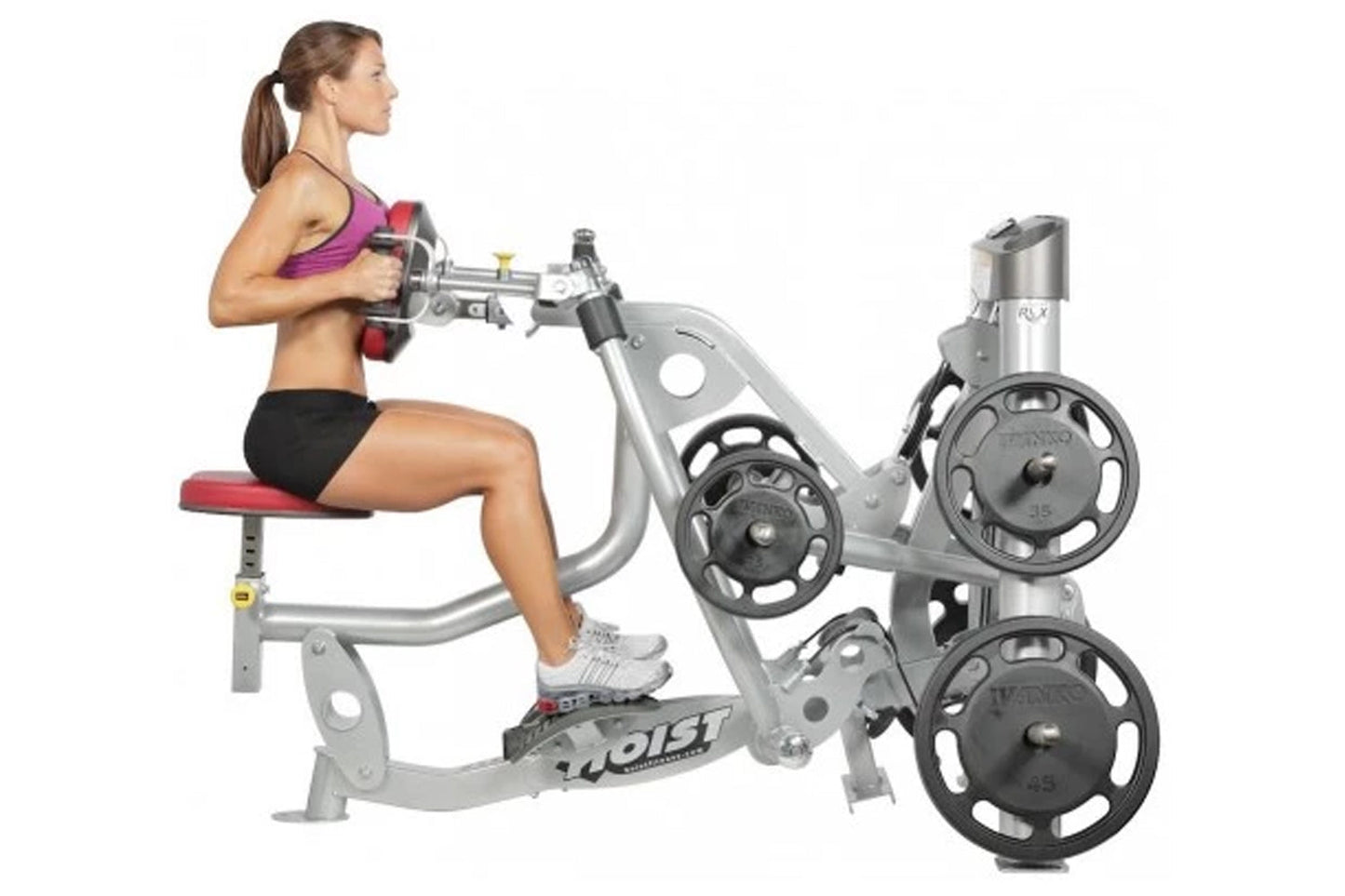Woman in purple sports bra and black shorts using Hoist ROC-IT seated mid row machine with weight plates, shown in profile on