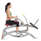 Woman in green sports bra and black capris using silver Hoist seated calf raise machine with foot pedal on white background