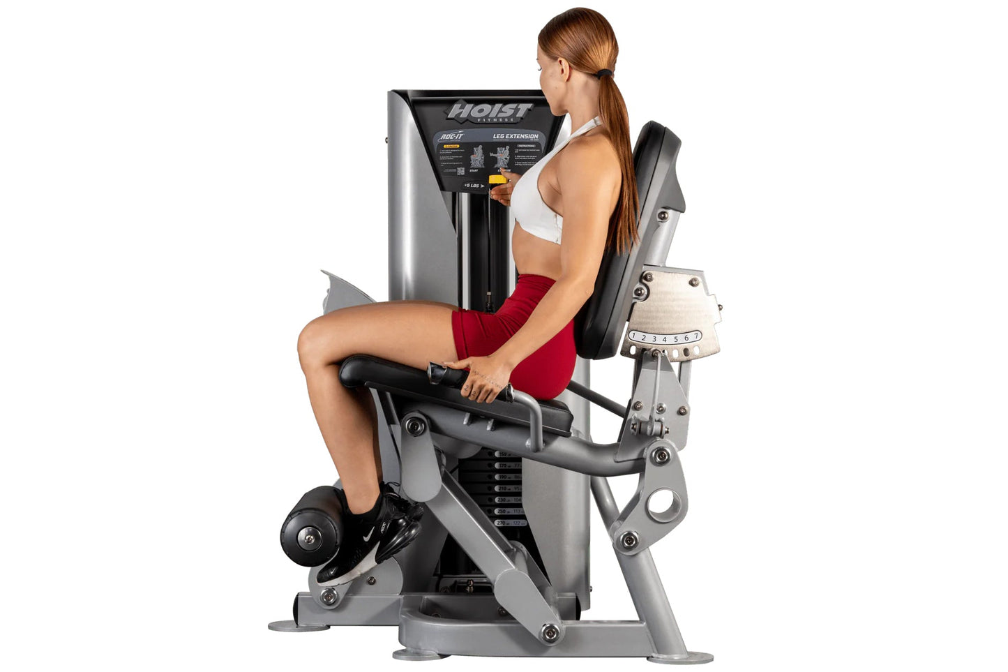 Woman using Hoist ROC-IT leg extension machine with silver frame and black seat, demonstrating proper form on white backgroun
