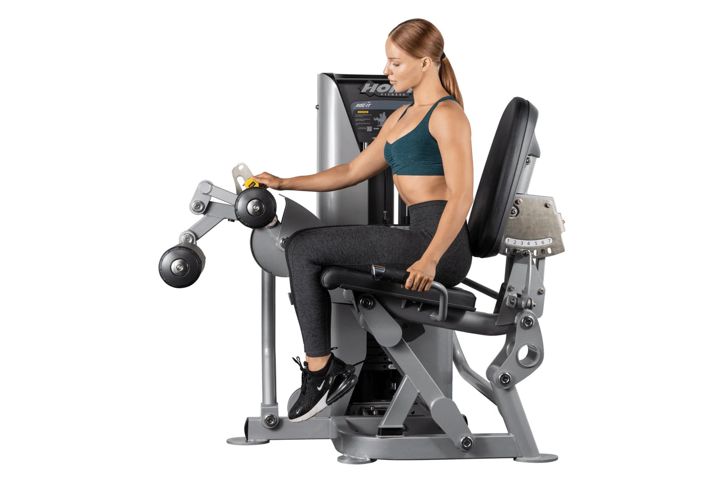 Woman using Hoist ROC-IT leg curl machine with dumbbells, silver and black fitness equipment on white background