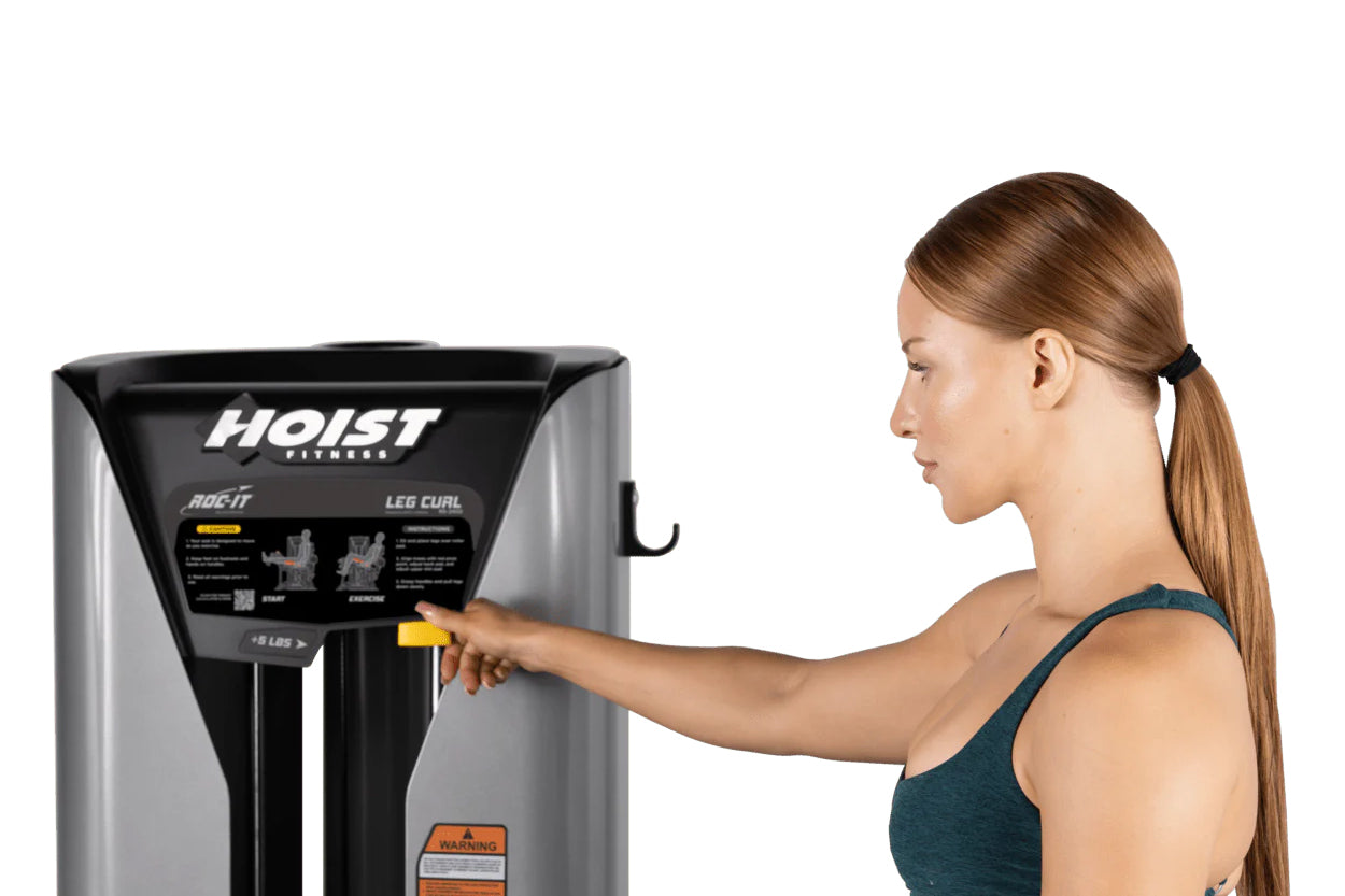 Woman with brown hair using black and silver Hoist ROC-IT leg curl machine with yellow controls