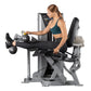 Woman using silver and black leg curl machine while holding dumbbells, demonstrating exercise position on white background