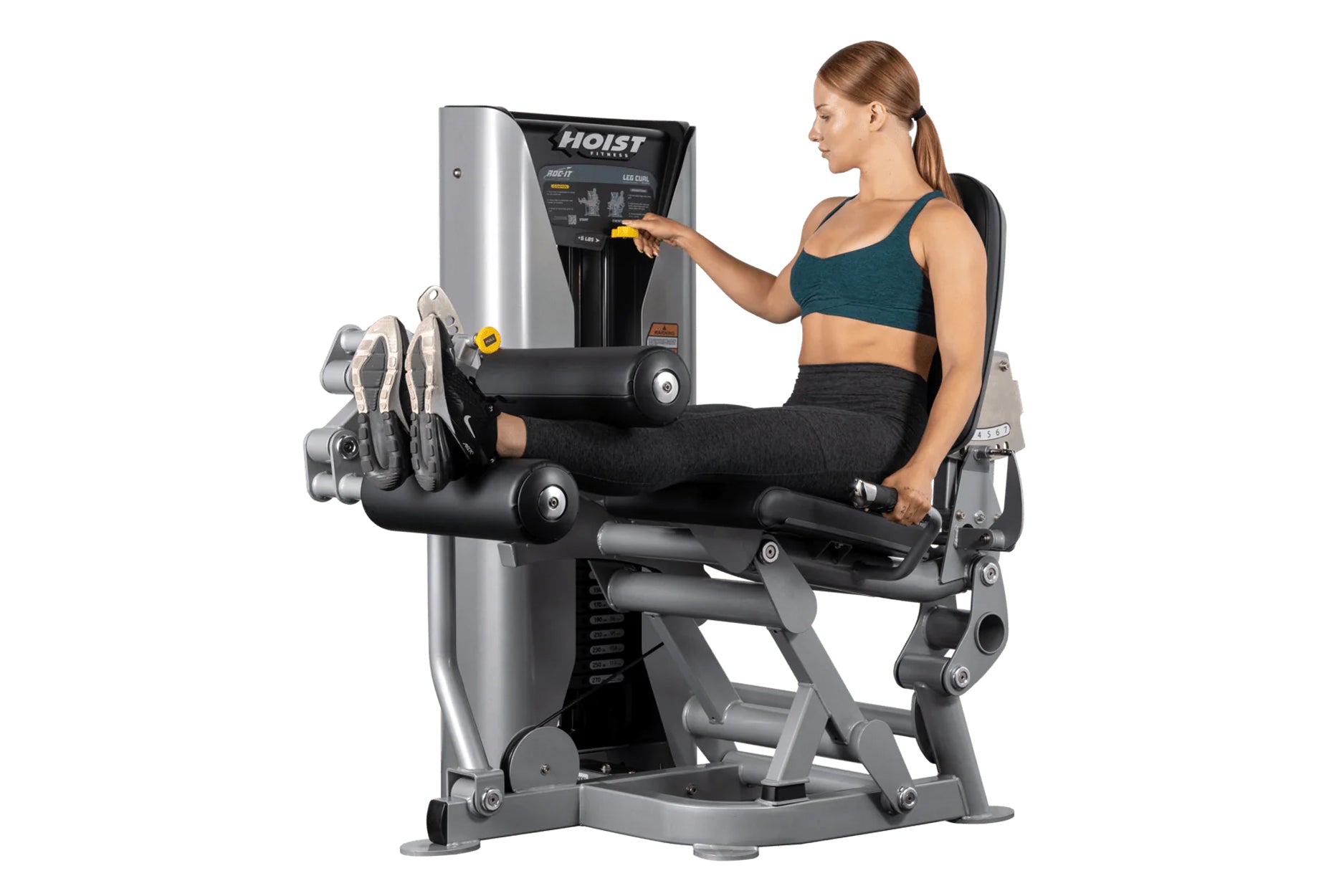 Woman in teal sports bra and black leggings using silver and black Hoist leg curl machine with digital display