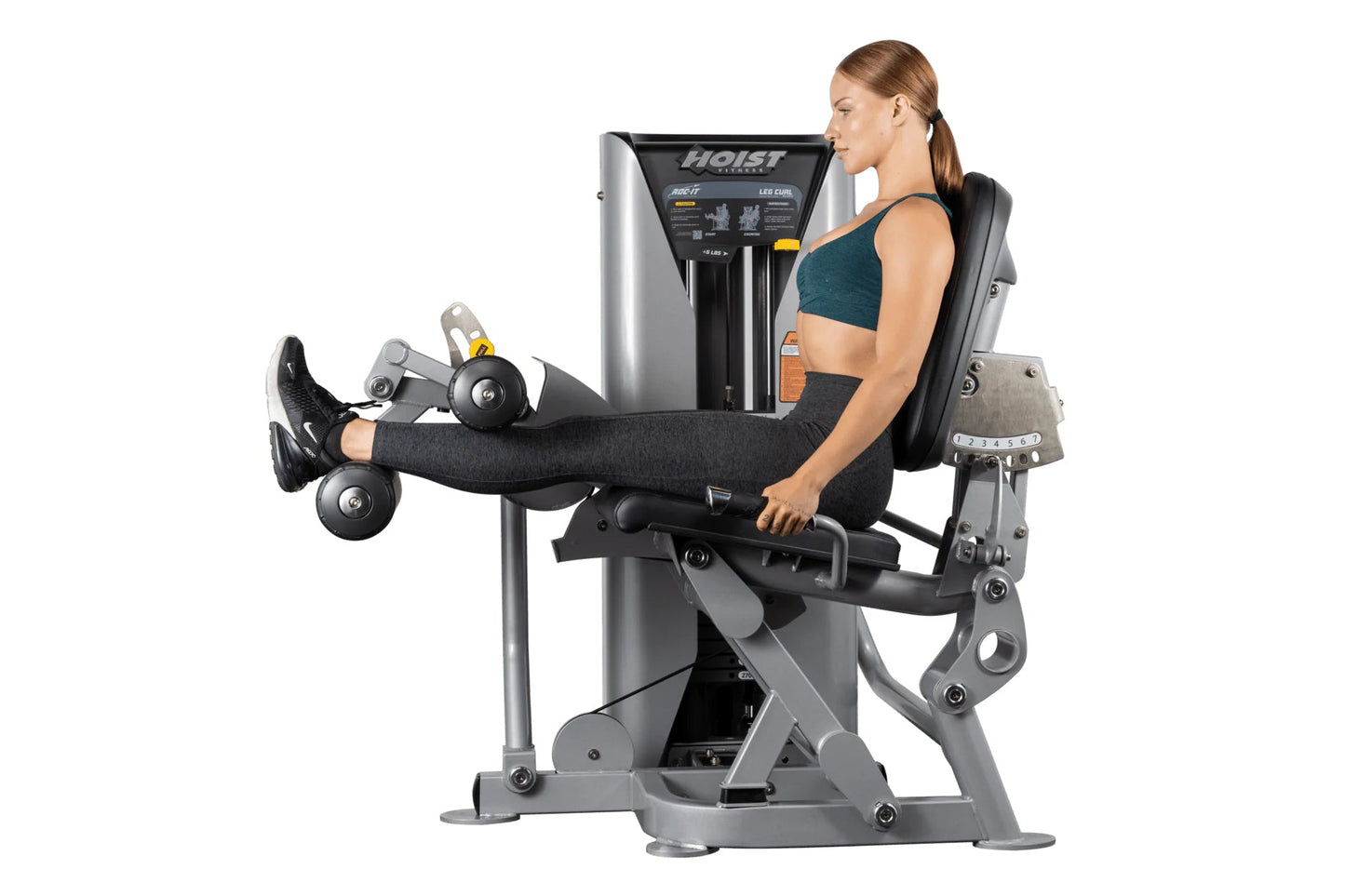 Woman using Hoist ROC-IT leg curl machine with silver and black frame, demonstrating leg extension exercise position