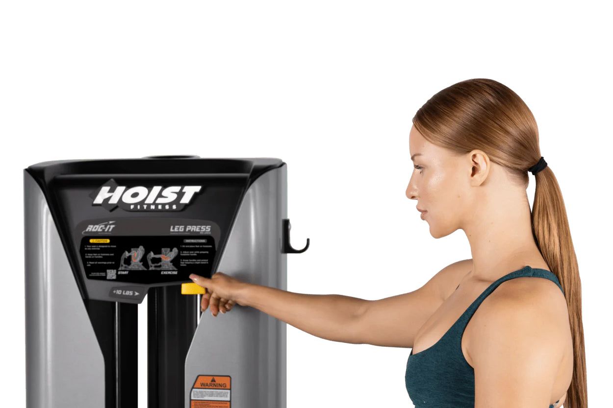 Woman in teal tank top using Hoist ROC-IT leg press machine with black and silver frame on white background