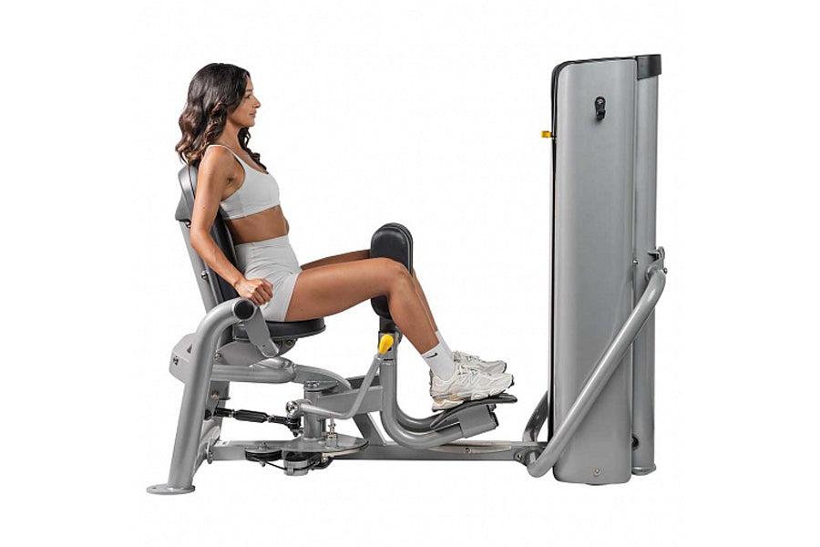Woman using gray Hoist ROC-IT leg exercise machine with padded seat and footrest, shown in side profile on white background