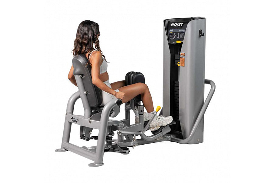 Woman using gray and black Hoist leg press machine with padded seat and footrest on white background