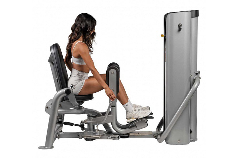 Woman seated on gray Hoist ROC-IT leg press machine with padded backrest and foot platform, demonstrating proper form on whit