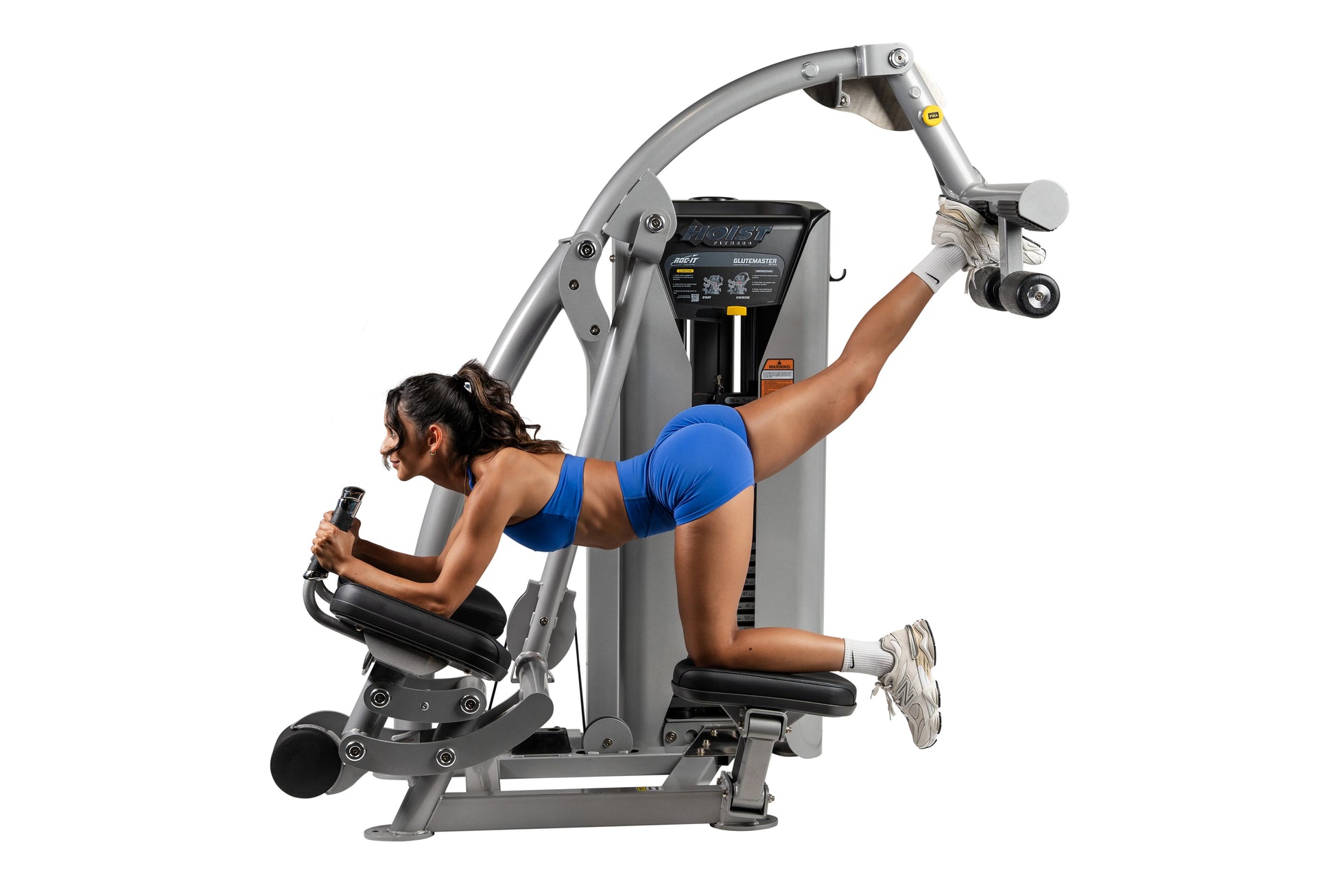 Woman in blue sports bra using gray Hoist ROC-IT Glute Master exercise machine with black seat and controls on white backgrou