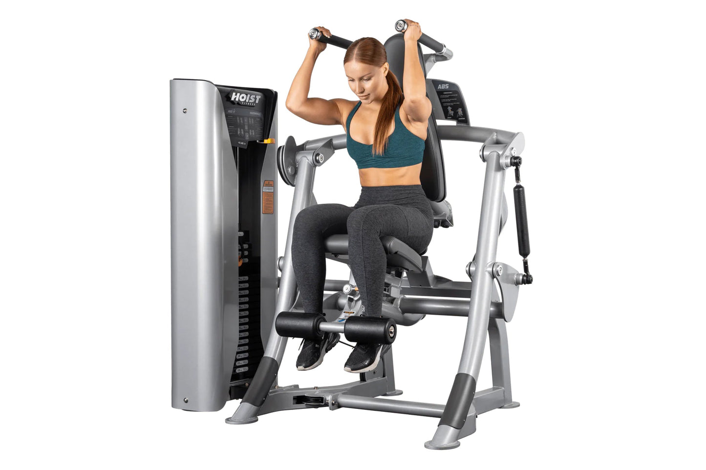 Woman using Hoist ROC-IT abs machine with silver frame and black padding, holding dumbbells overhead on white background