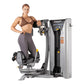 Woman in brown sports bra and gray leggings using Hoist ROC-IT rotary torso machine with silver and black frame on white back