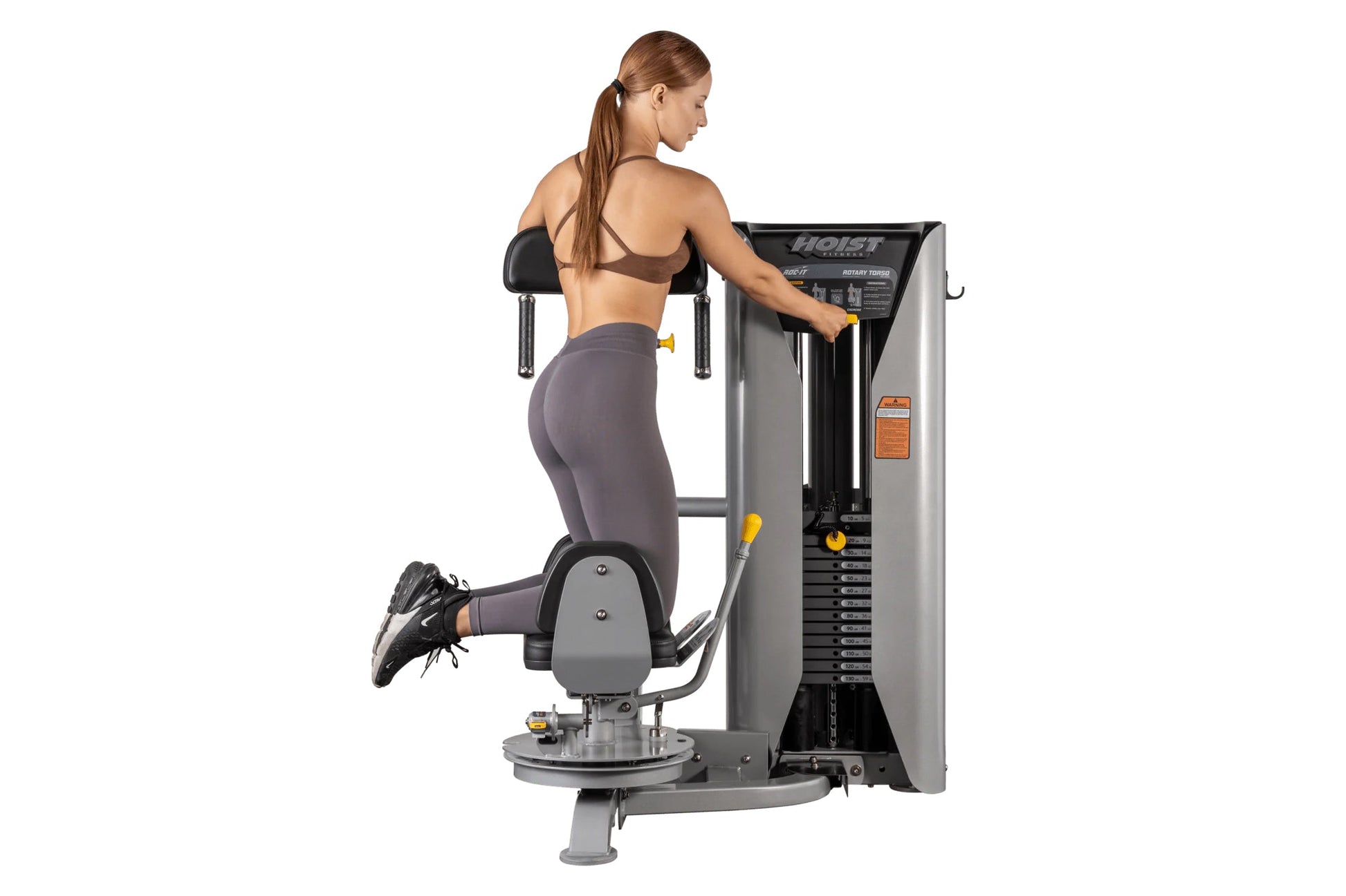 Woman using gray and black Hoist rotary torso exercise machine with yellow handles, shown from side view on white background