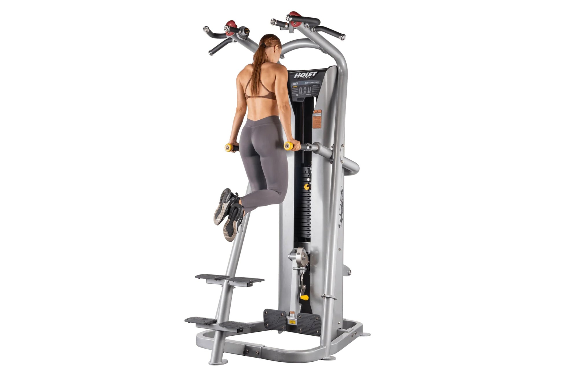 Woman using silver Hoist ROC-IT chin/dip assist machine with dual handles and yellow weight plates on white background