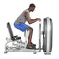 Man using leg press machine with gray frame and white seat, blue shorts, demonstrating inner and outer thigh exercise equipme