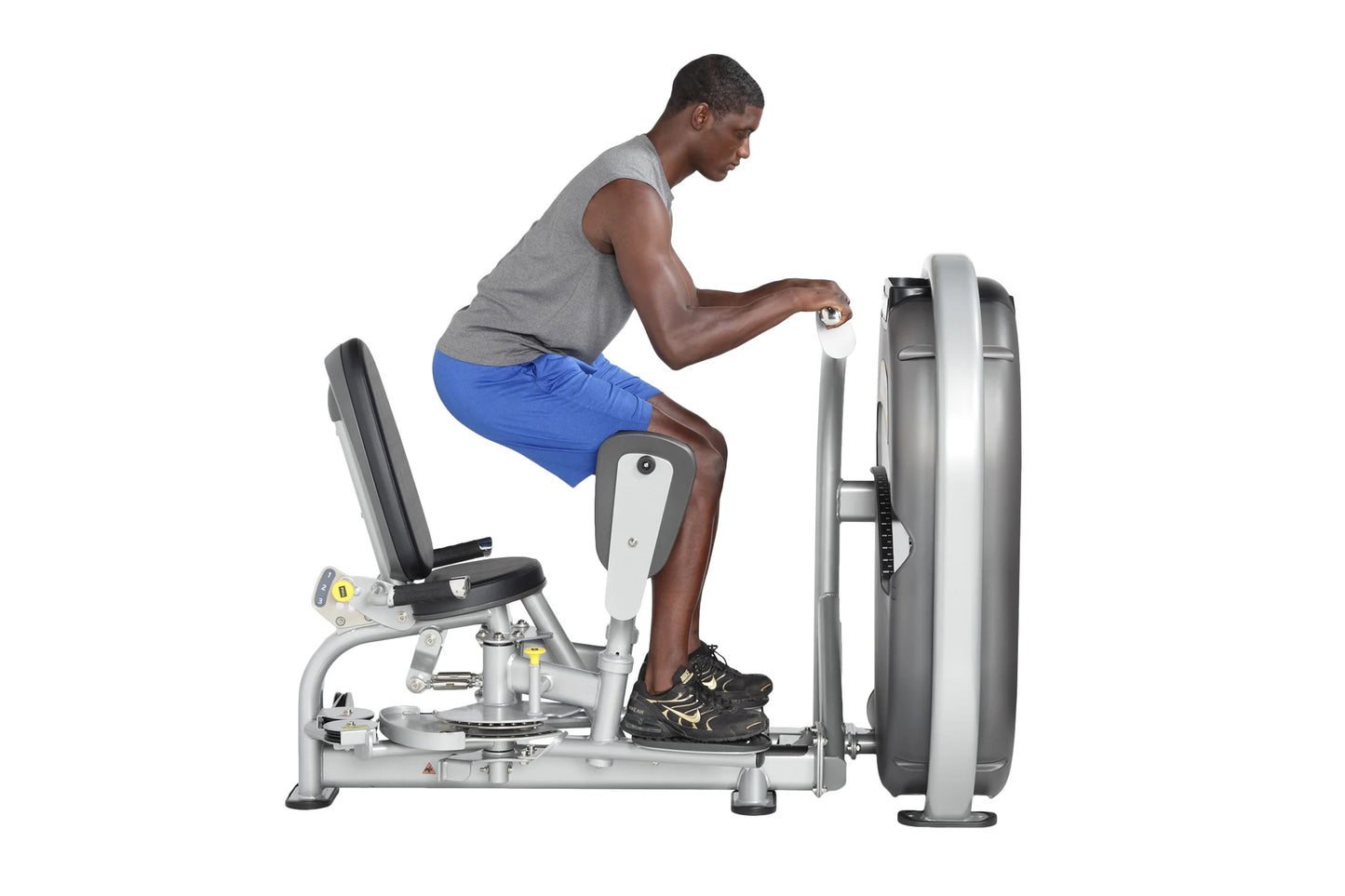 Man using leg press machine with gray frame and white seat, blue shorts, demonstrating inner and outer thigh exercise equipme