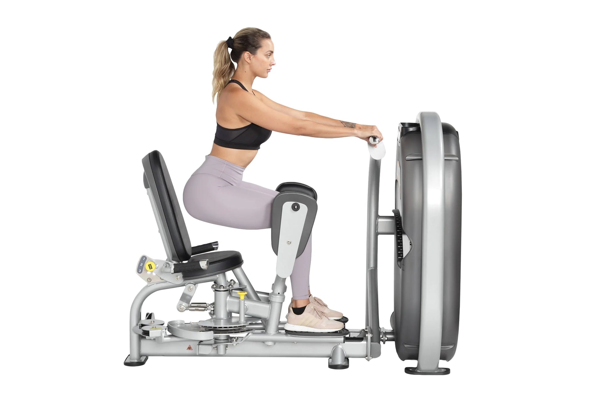 Woman using silver and black leg press machine with padded seat, worn by model in black sports bra and lavender leggings on w