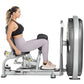 Woman using silver and black leg press machine with large weight plate, wearing black sports bra and lavender leggings