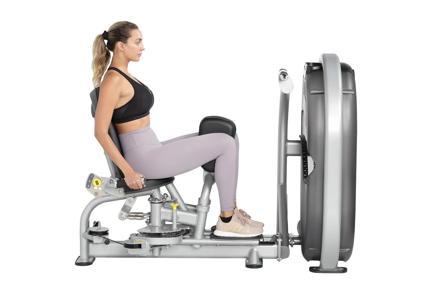 Woman using silver and black leg press machine with large weight plate, wearing black sports bra and lavender leggings