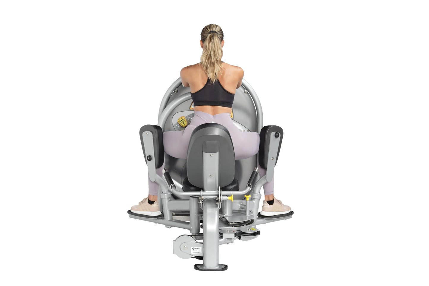 Woman using gray and black inner/outer thigh exercise machine, viewed from behind, on white background
