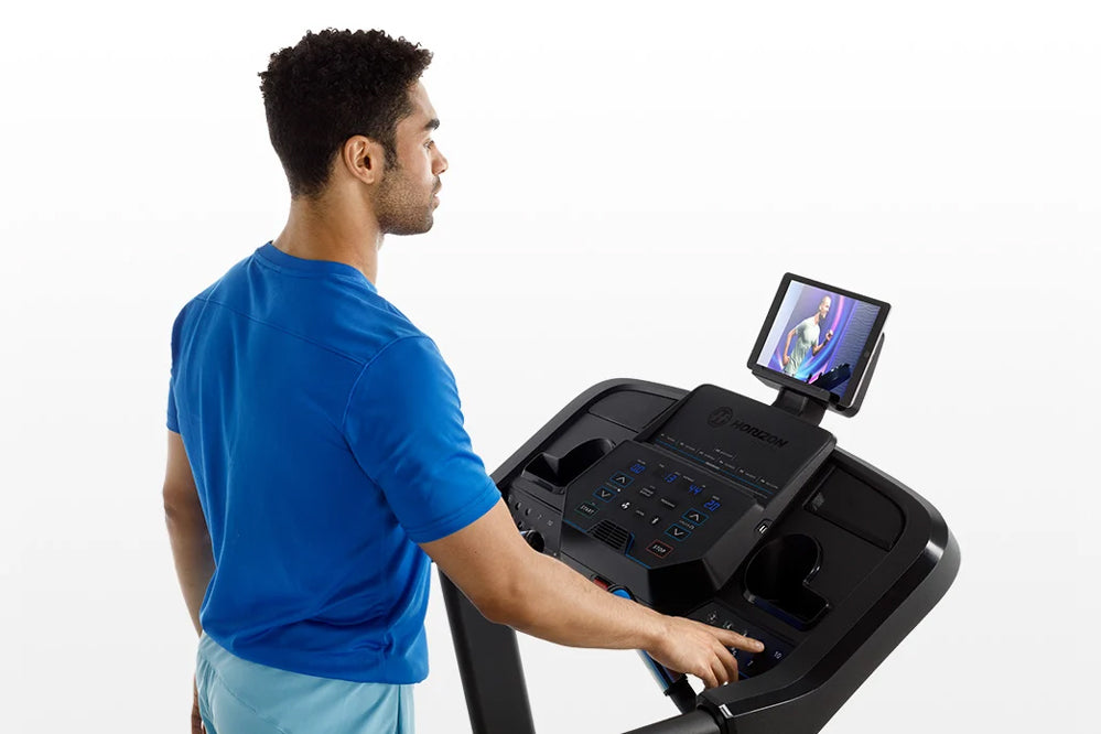 Man in blue t-shirt using black Horizon 5.0 AT treadmill with tablet display, side view on white background