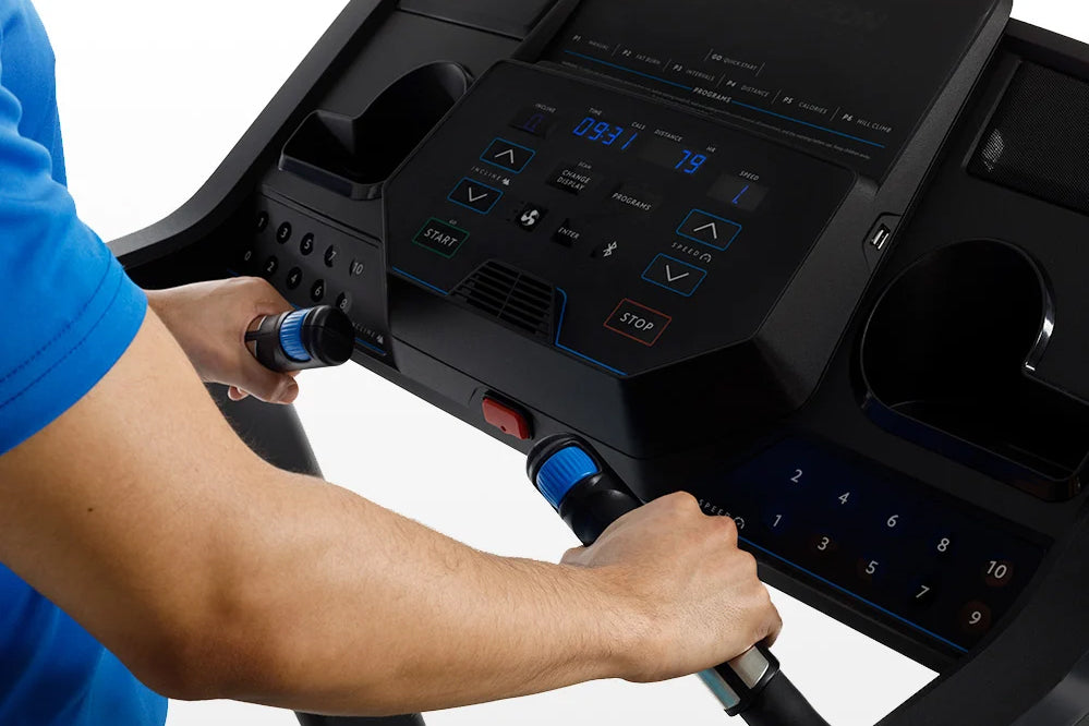 Person in blue shirt operating black treadmill console with blue-lit digital display and dual handlebar controls