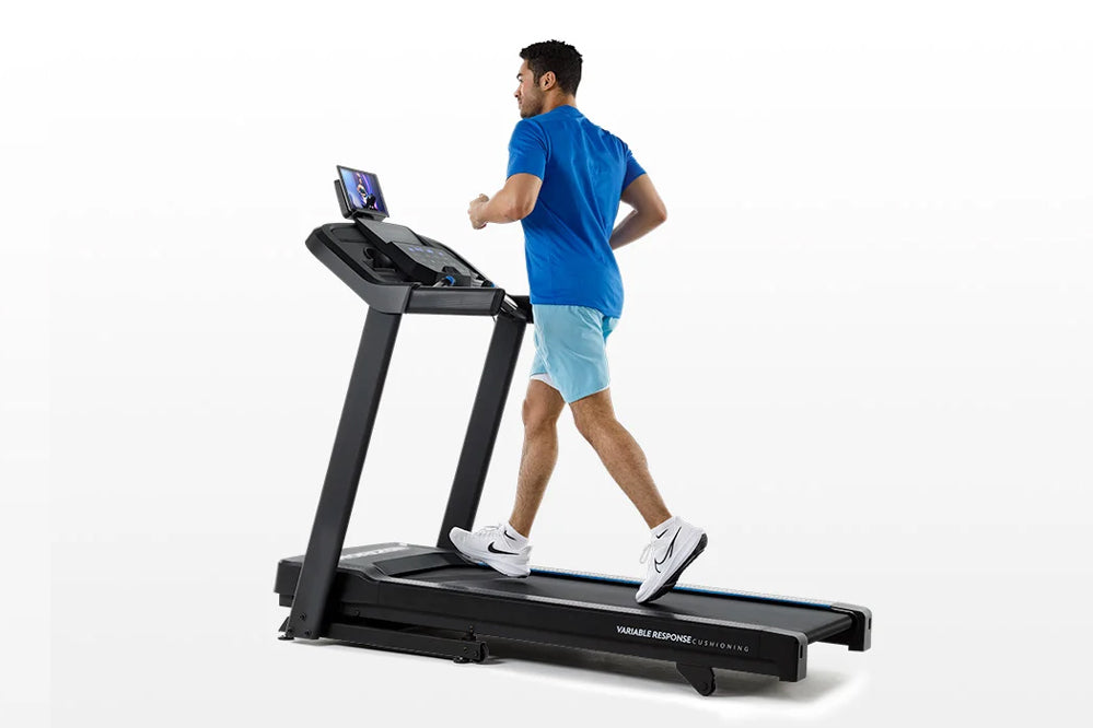 Man jogging on black Horizon 5.0 AT treadmill with blue touchscreen display, wearing blue t-shirt and light blue shorts