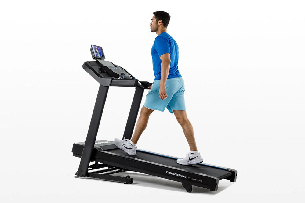 Man wearing blue t-shirt and light blue shorts running on black Horizon 5.0 AT treadmill with digital display on white backgr