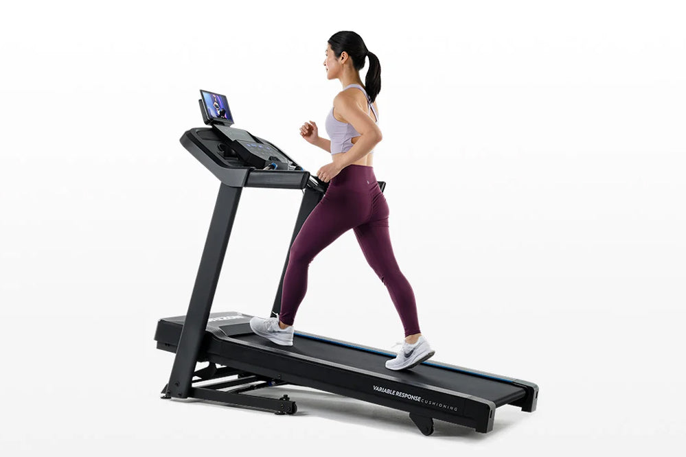 Woman running on black Horizon 5.0 AT treadmill with digital display, wearing lavender sports bra and burgundy leggings