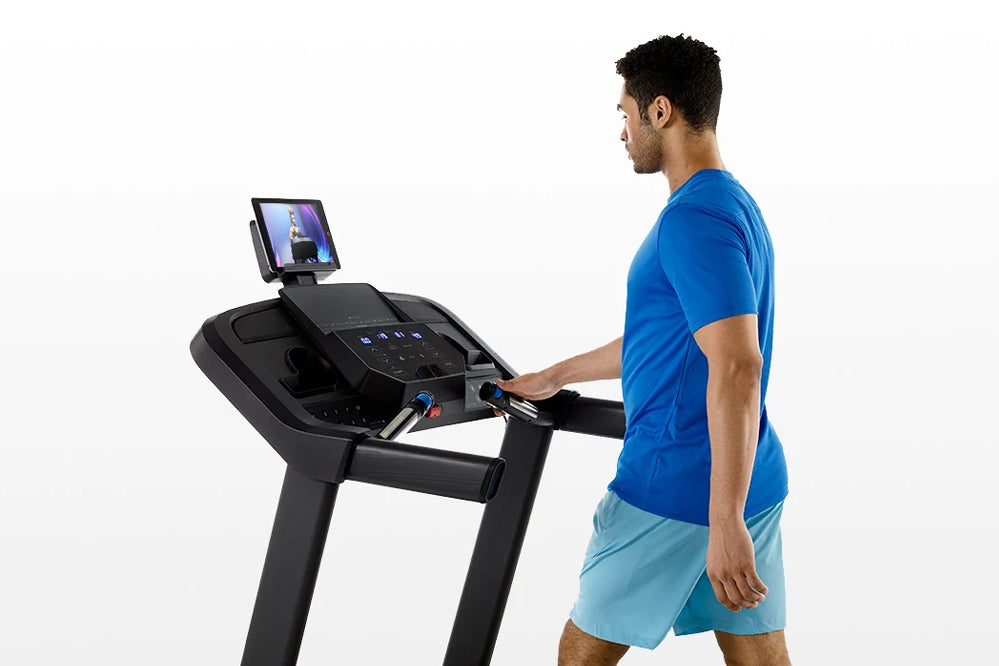 Man in blue t-shirt using black Horizon 5.0 AT treadmill with display screen, shown from side view on white background