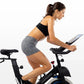 Woman in black sports bra and gray shorts on black Horizon 5.0 IC stationary bike holding tablet, shown in profile against wh