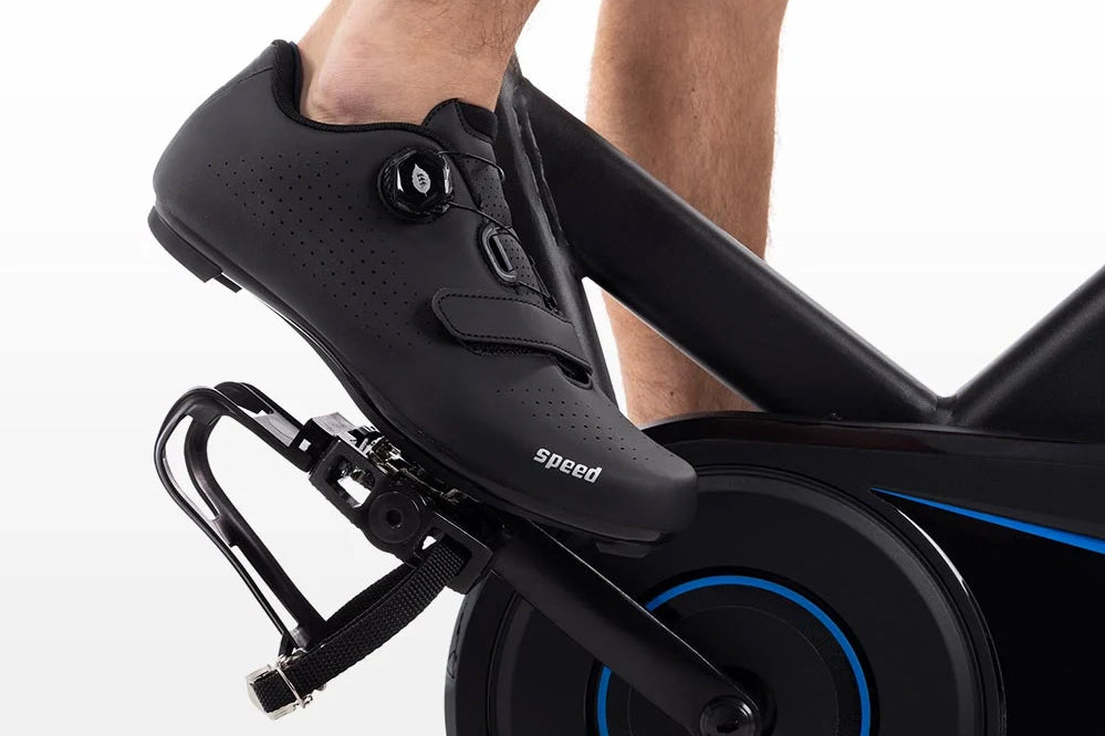 Black cycling shoe with perforated leather upper and dial closure system, worn on stationary bike pedal