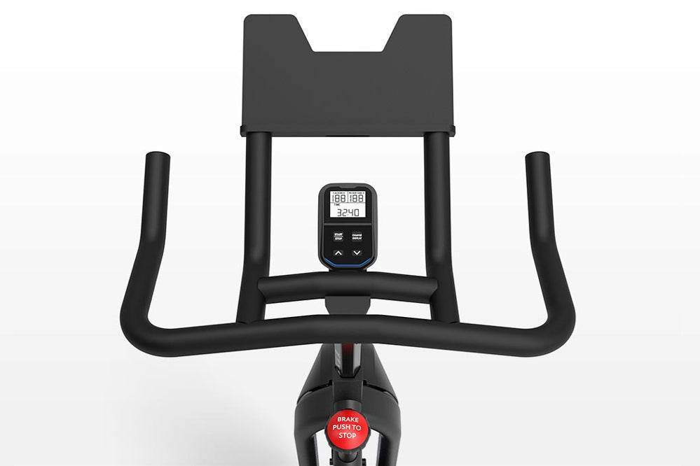 Black indoor exercise bike with curved handlebars, digital display console, and red brake button on white background