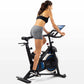 Woman in black sports bra and gray shorts riding black and blue stationary exercise bike with tablet holder on white backgrou