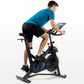 Man wearing bright blue t-shirt and black shorts riding black and blue stationary exercise bike with tablet holder, shown on 
