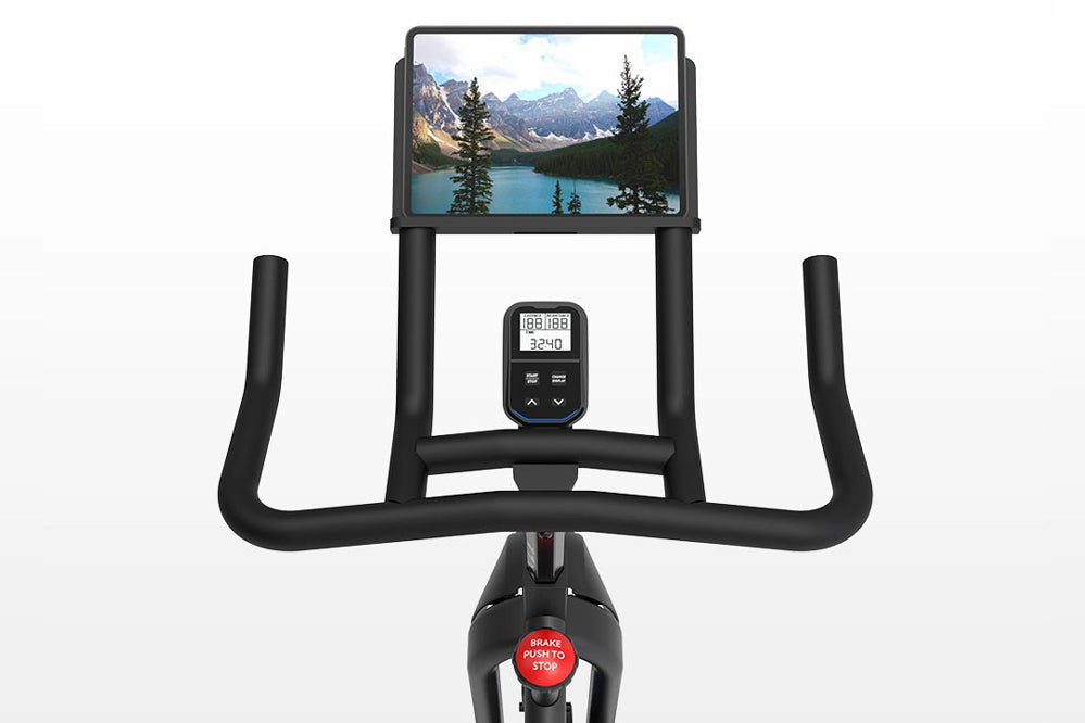 Black indoor stationary bike with tablet holder displaying mountain landscape, digital console showing metrics, and curved ha