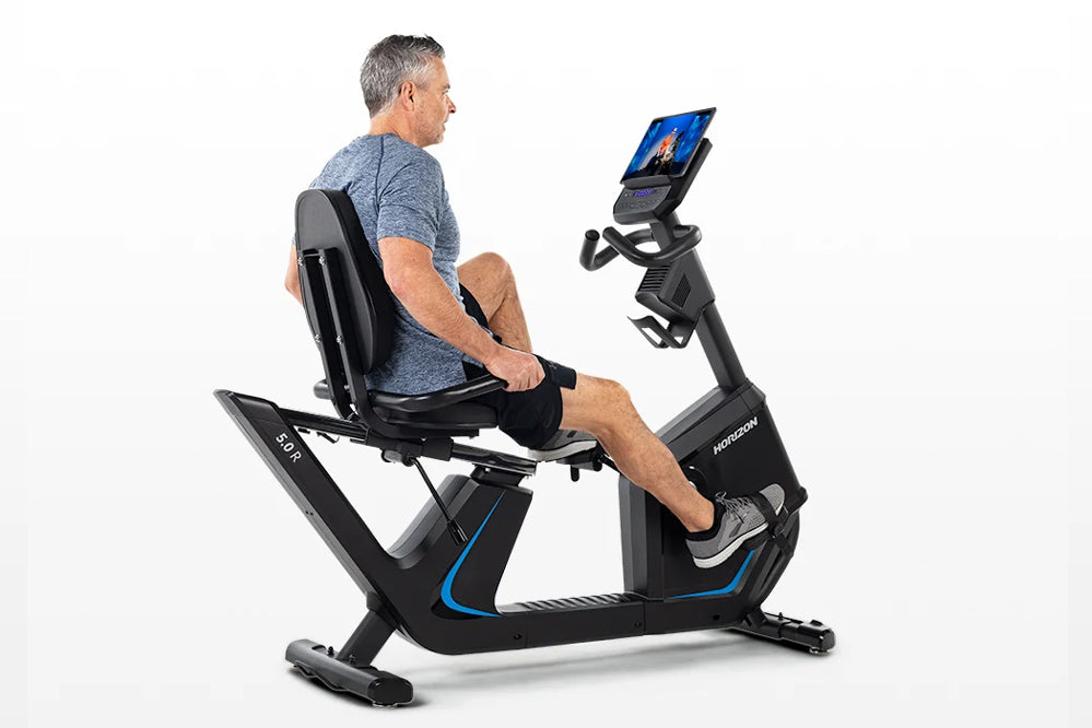 Middle-aged man in gray shirt and black shorts using black Horizon recumbent exercise bike with blue accents and blue display