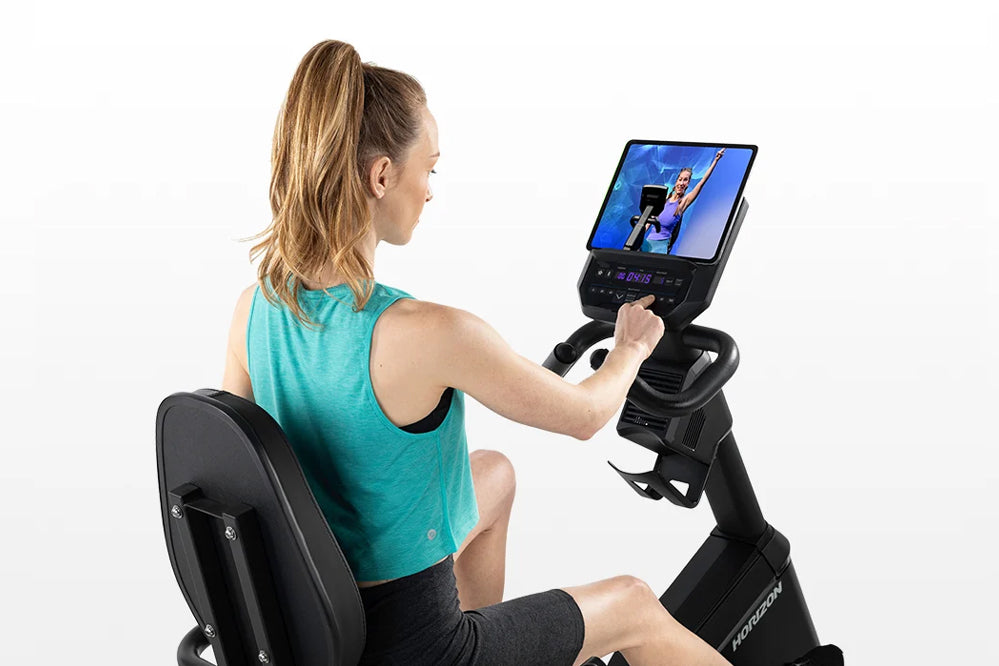 Woman in teal tank top using Horizon 5.0 R recumbent exercise bike with digital display screen on white background