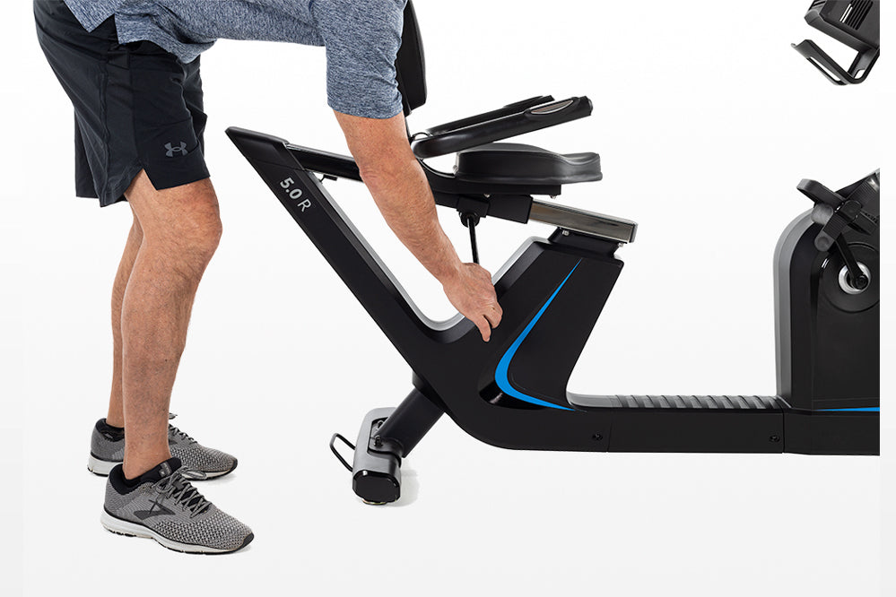 Man using black recumbent exercise bike with blue accent details and adjustable seat, worn with navy shorts and gray sneakers