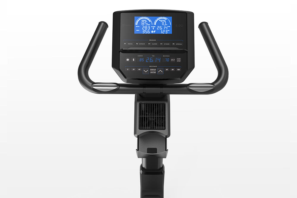 Black upright exercise bike with curved handlebar grips, digital console displaying blue screen metrics, and pedal base, on w